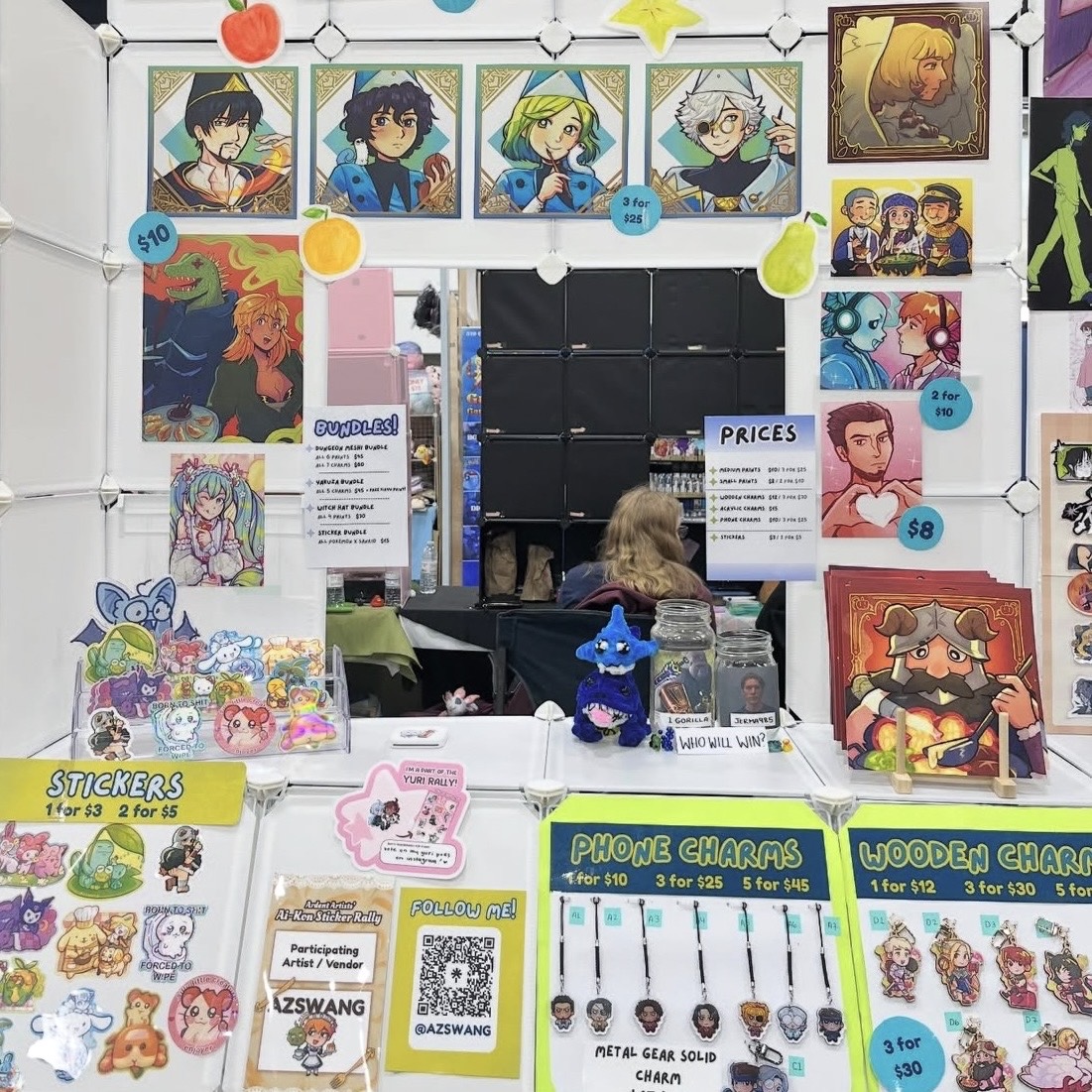 Anime and game fan art booth with character prints, stickers, wooden charms, phone charms, price signs, and a QR code for the artist.