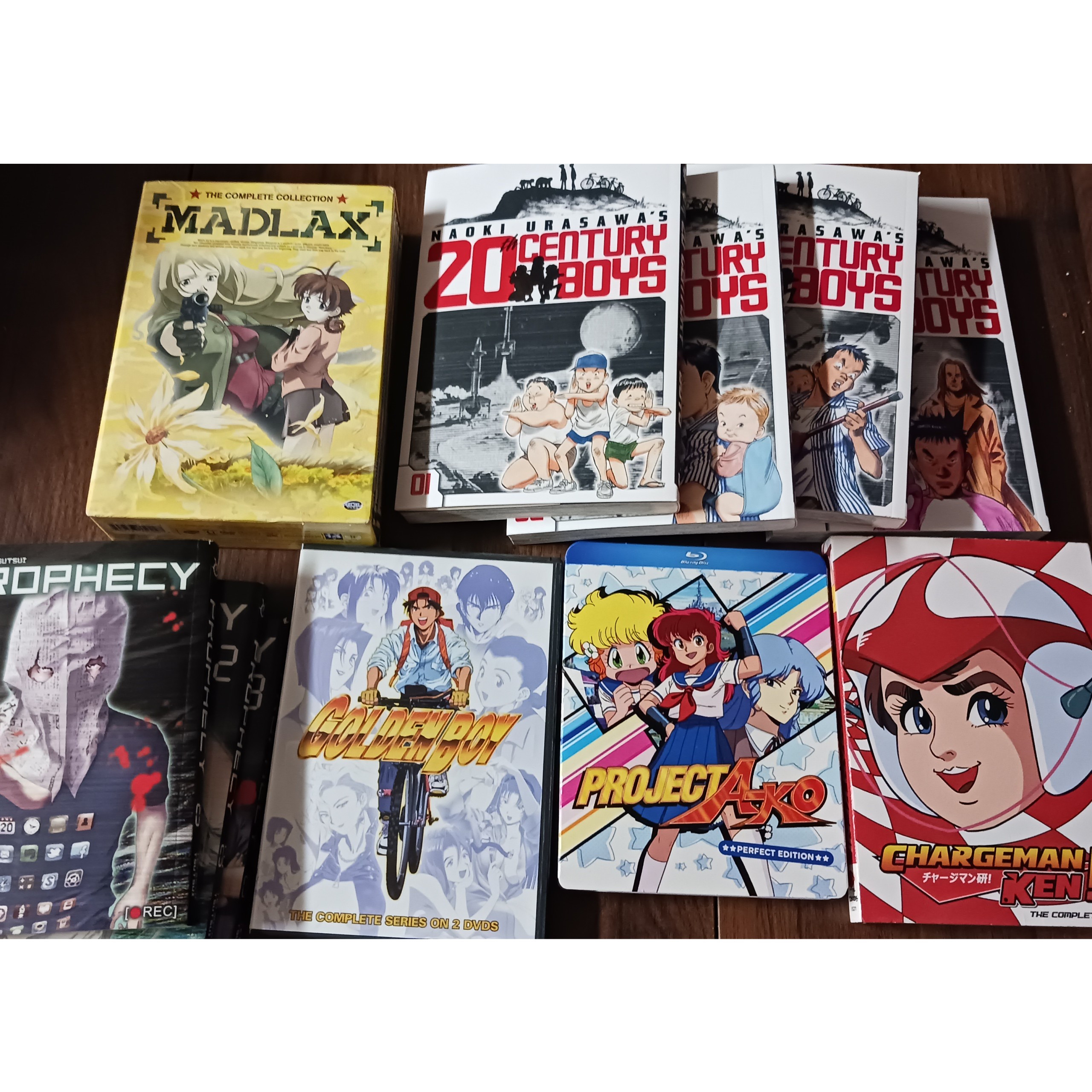 Selection of used anime DVDs, Blu-rays, and manga arranged on a tabletop, including Madi-lax, 20th Century Boys, Golden Boy, Project A-Ko, and Chargeman Ken.