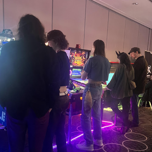 Attendees playing illuminated arcade rhythm games in a dim convention game room.