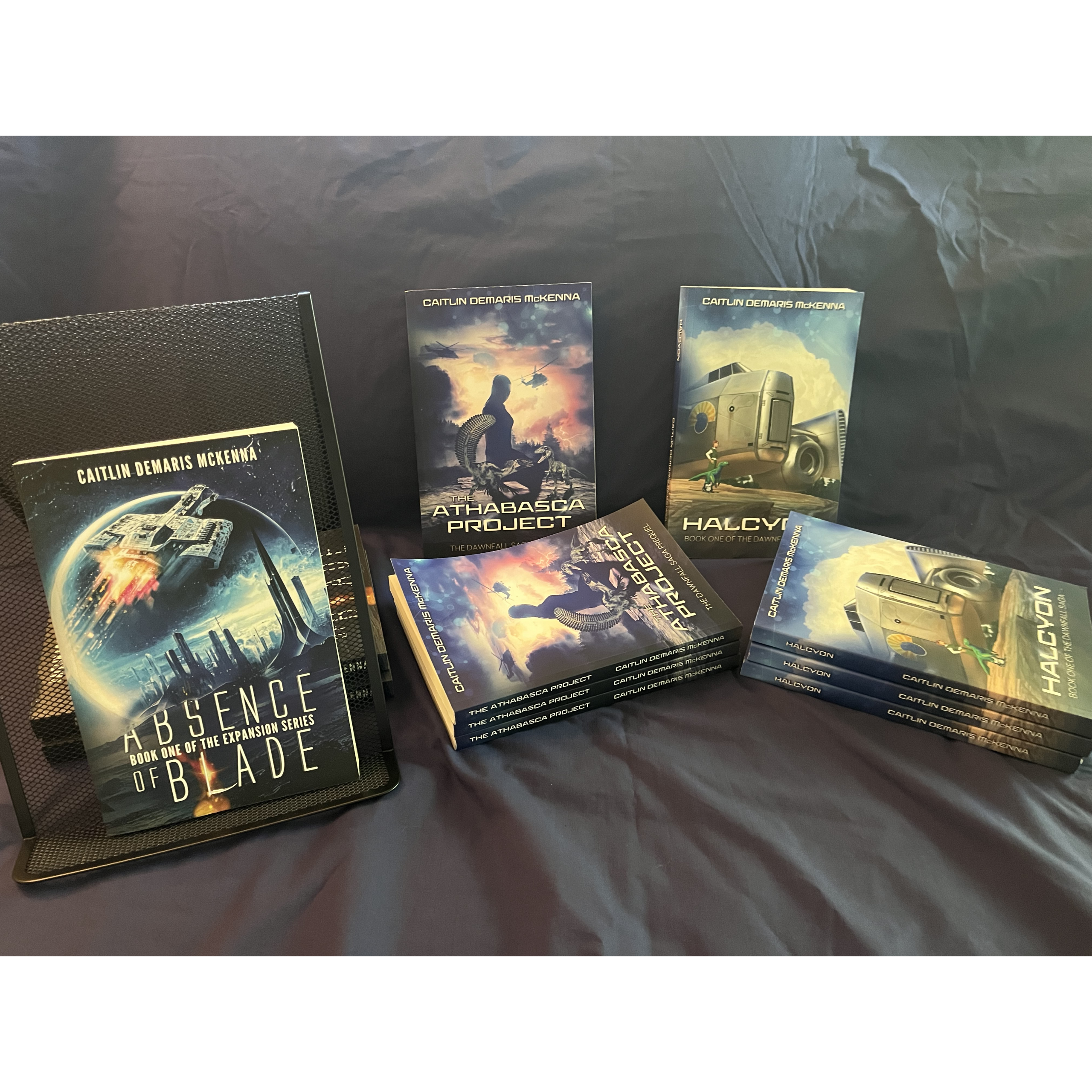 Display of Caitlin McKenna sci-fi novels on a black tablecloth, including Absence of Blade, The Athabasca Project, and Halcyon.