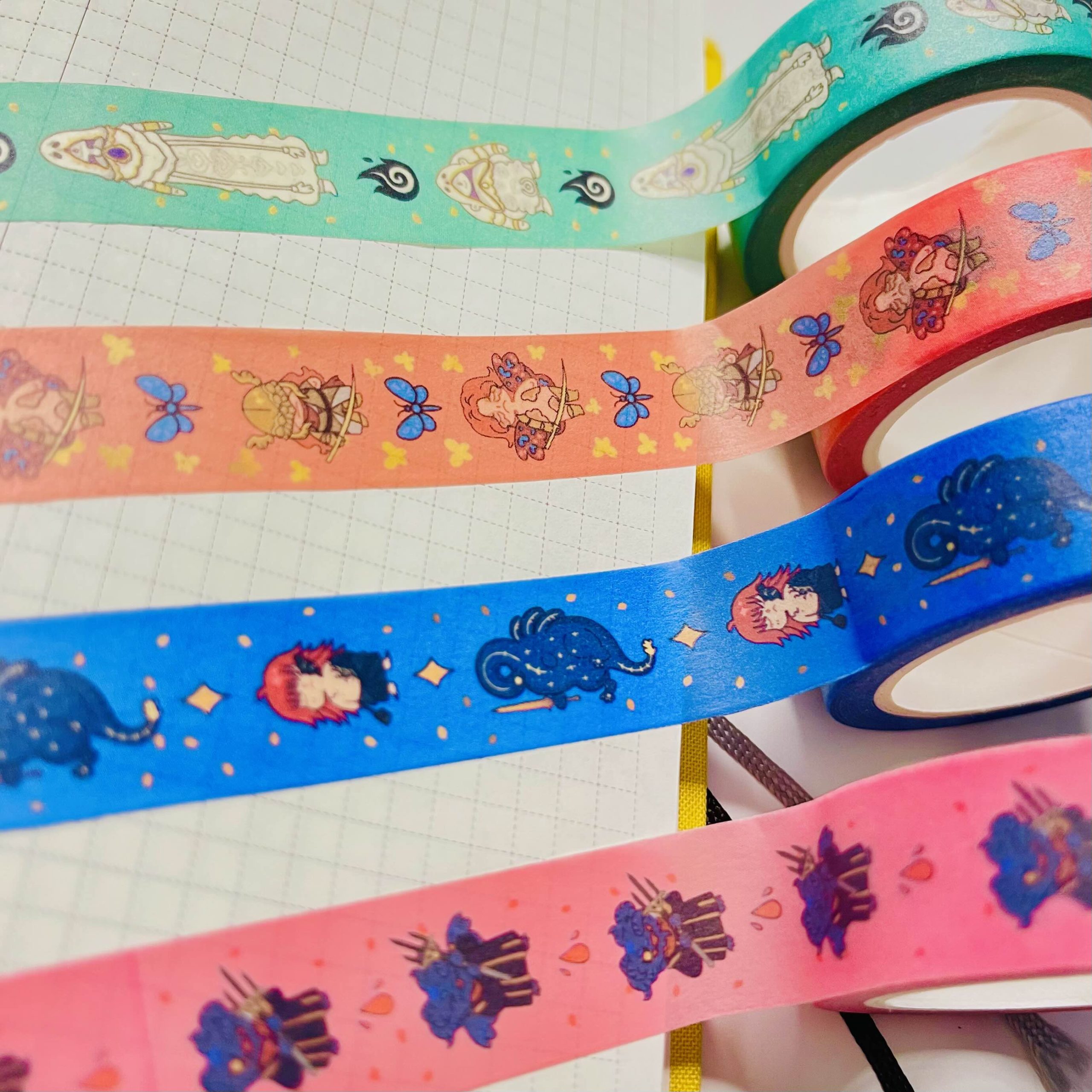 Close-up of colourful washi tape rolls with tiny illustrated characters and motifs in teal, coral, blue, and pink designs.