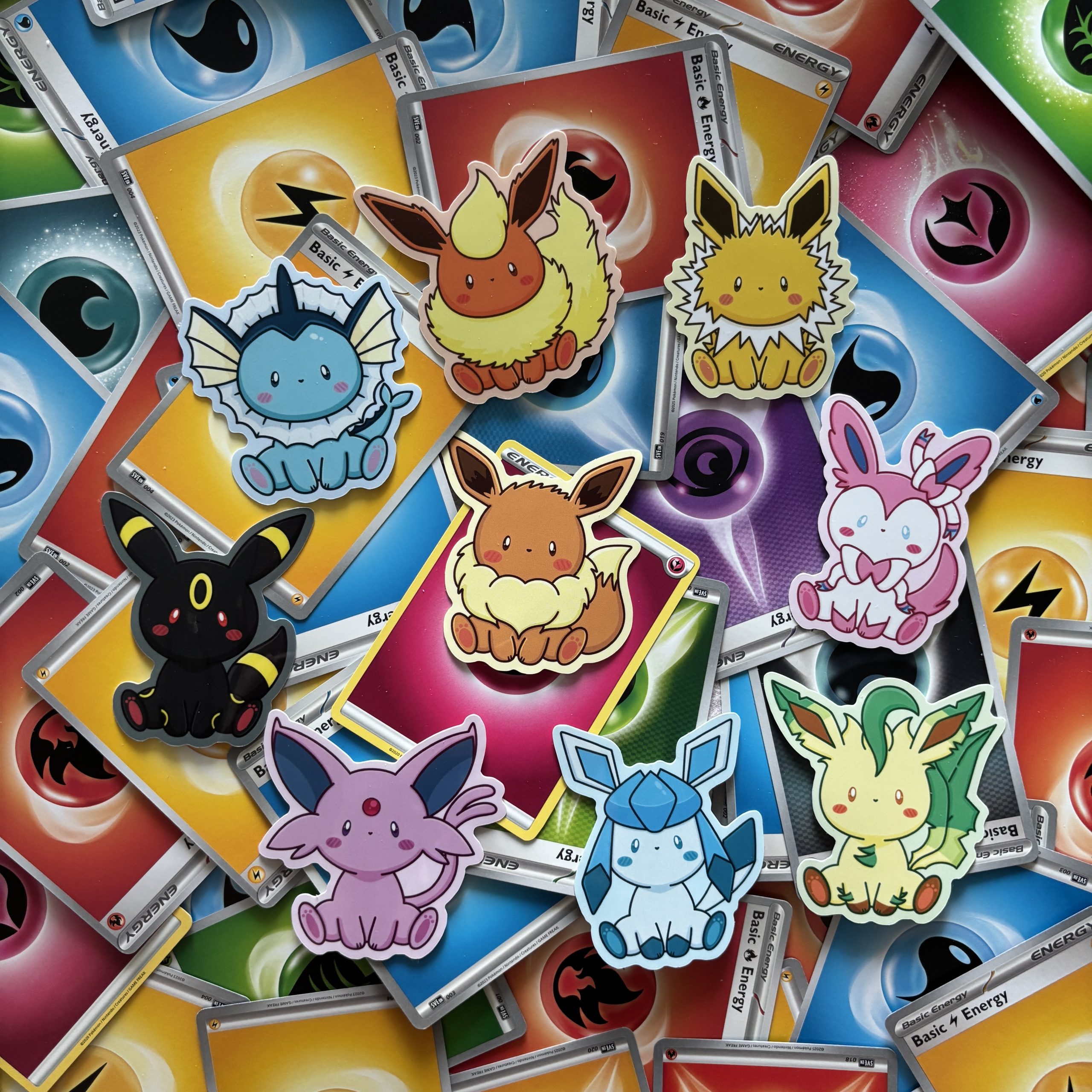 Cute Pokémon-inspired stickers of Eevee evolutions arranged on a background of colourful Pokémon energy cards.
