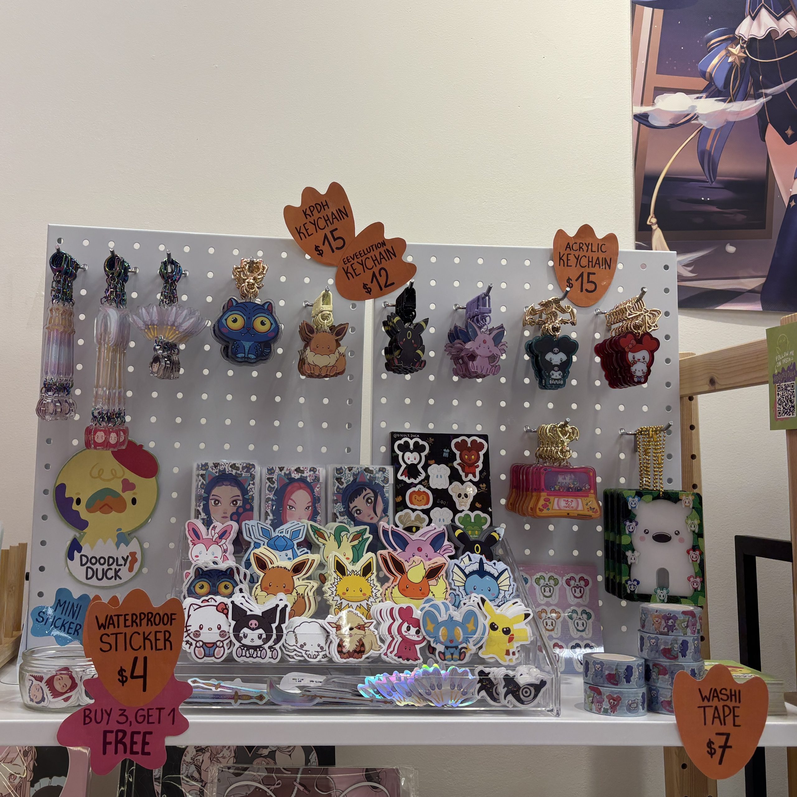 Vendor display of cute fan-made stickers, keychains, washi tape, and acrylic charms featuring Pokémon, Sanrio-style characters, and other colourful fandom designs.