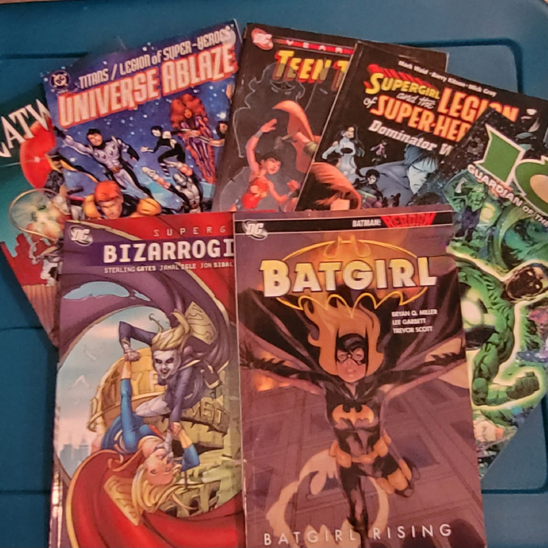Stack of DC comic books and graphic novels featuring Batgirl, Supergirl, Teen Titans, Green Lantern, and other superhero titles