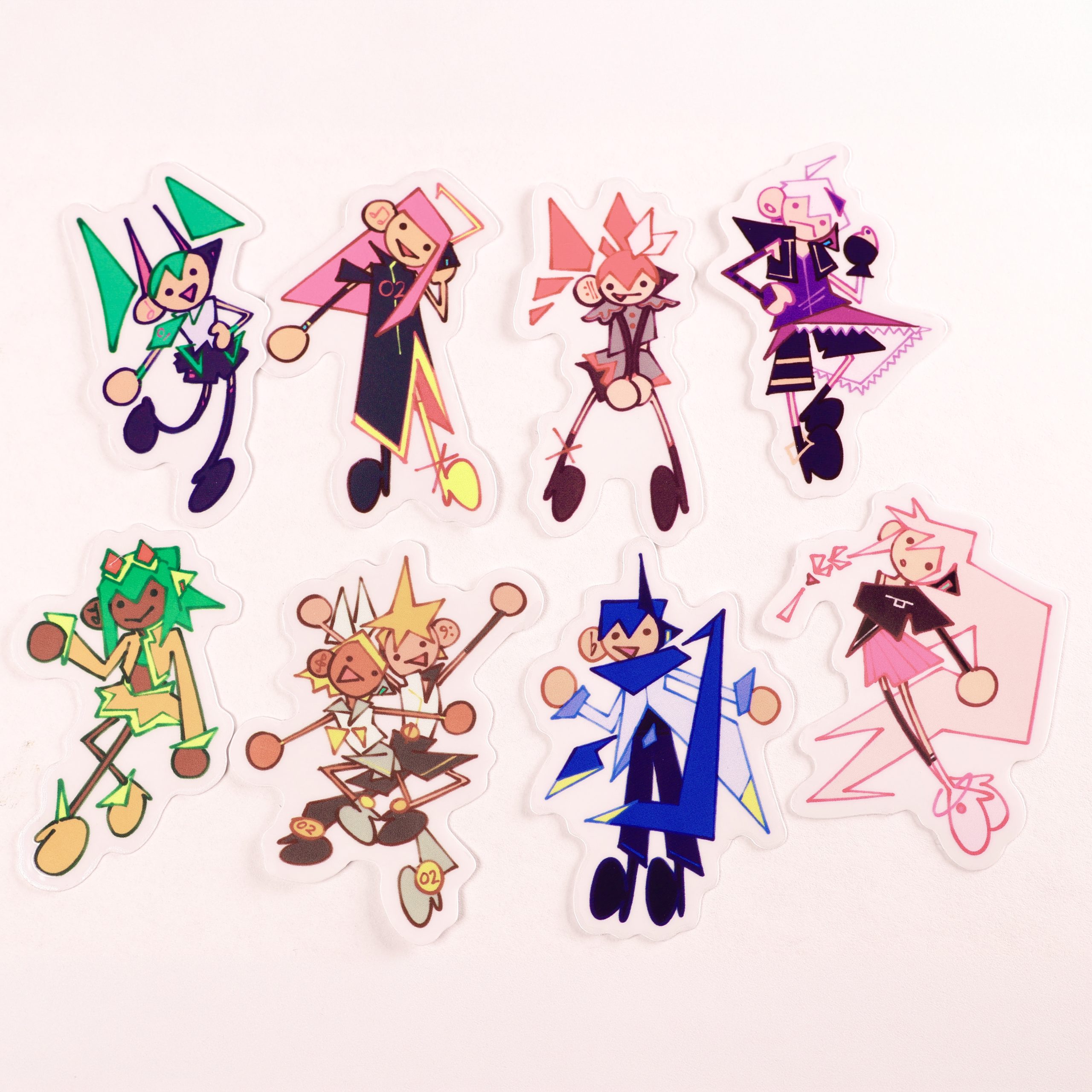 Seven colourful Vocaloid-themed acrylic stickers arranged on a pale background, featuring stylized angular character designs in bright green, pink, red, blue, and purple.