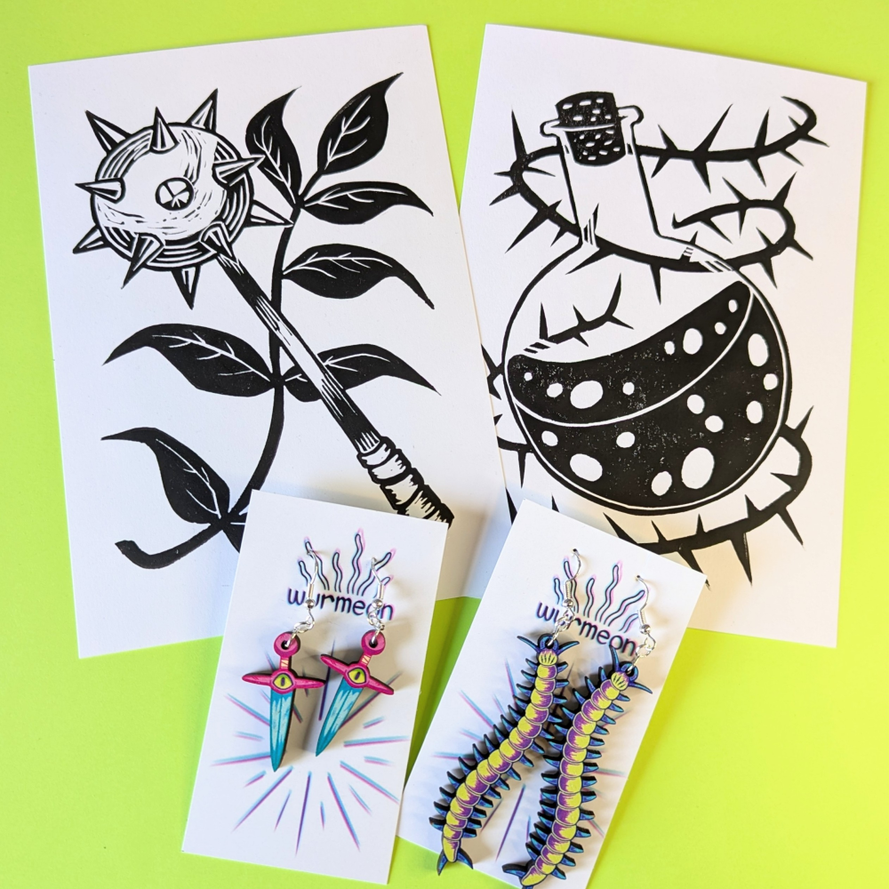 Two black-and-white fantasy lino-style prints with matching colourful earrings, including spiked flower, potion bottle, sword, and centipede designs.