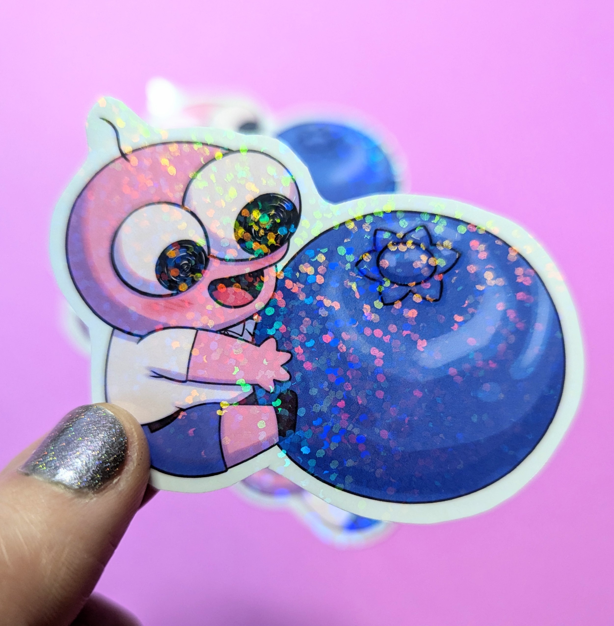 Glittery sticker of a wide-eyed cartoon creature hugging a large blue berry on a bright pink background.