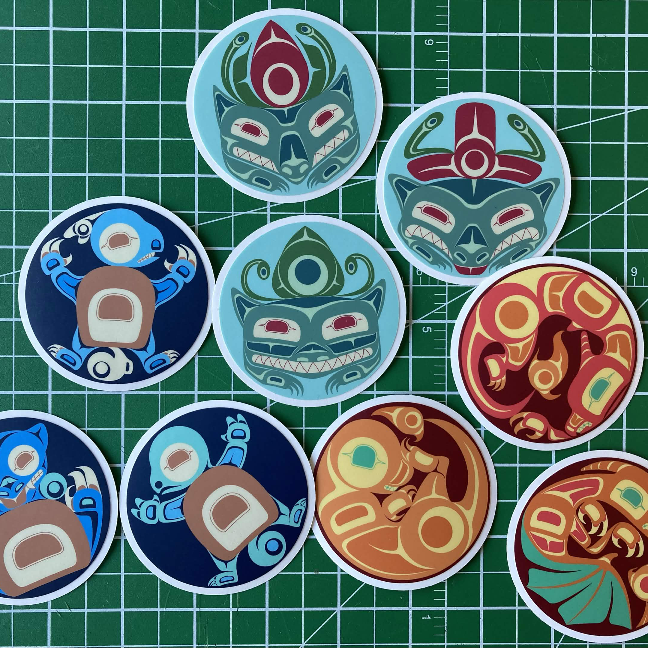 Round vinyl stickers on a green cutting mat featuring stylized animal designs in teal, blue, red, orange, and green colour palettes.