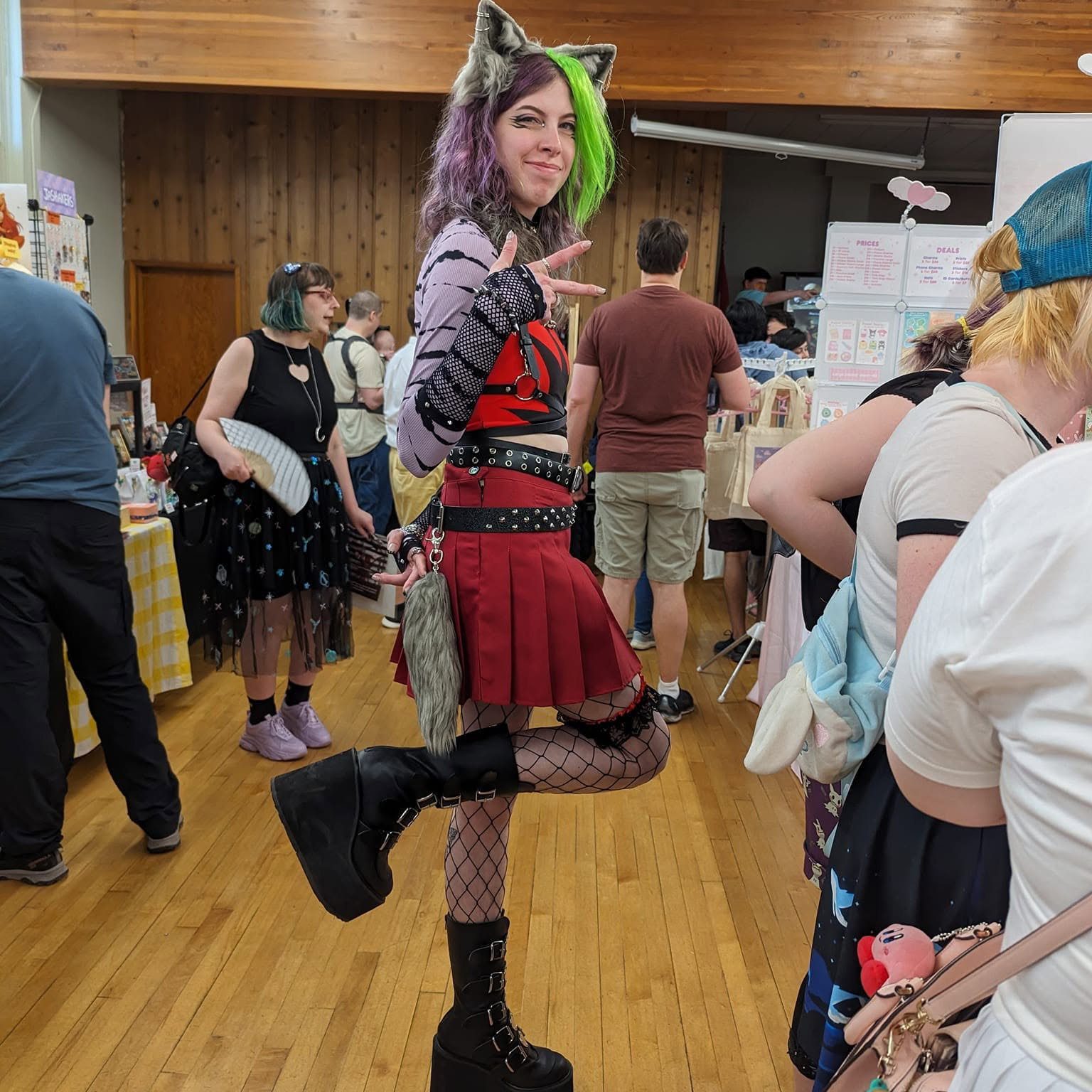 Cosplay attendee posing at Fandom Bazaar in a punk-inspired outfit with animal ears, bright green and purple hair, red skirt, and platform boots.