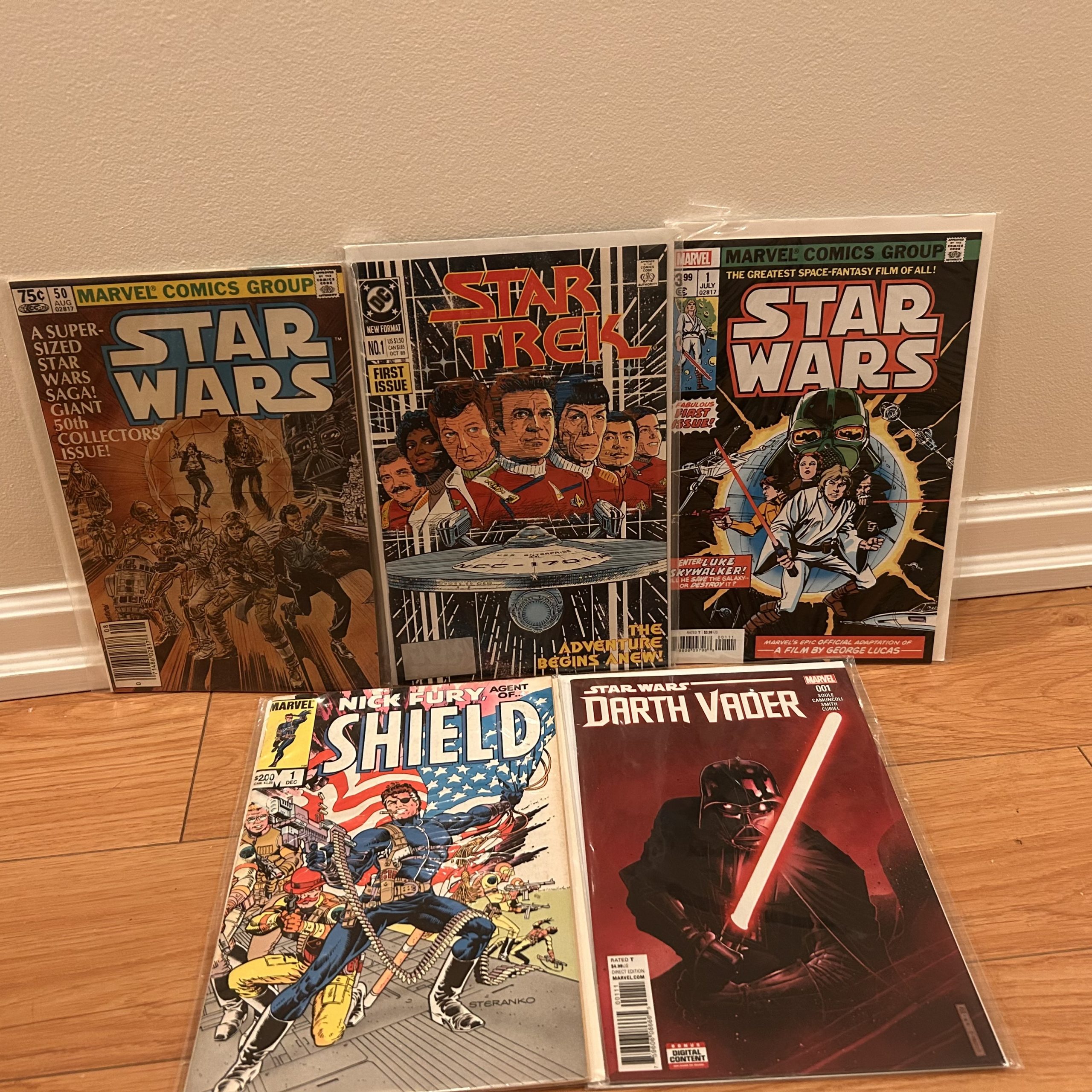 Selection of bagged comics featuring Star Wars, Star Trek, Nick Fury Agent of S.H.I.E.L.D., and Darth Vader issues displayed on a wood floor.